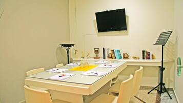 A conference room with a glass table, beige chairs, a mounted TV, a music stand, and a tripod.