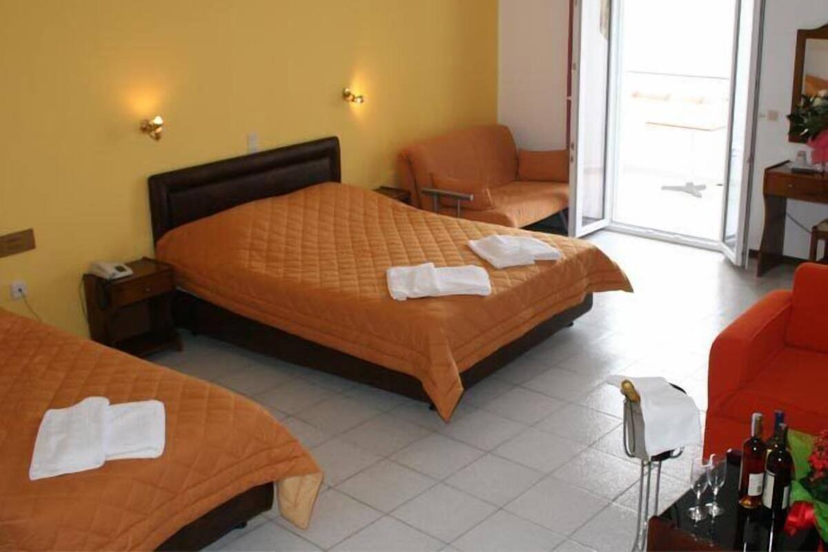 A hotel room with two beds, a sofa, a table with bottles, and a view of the outside.