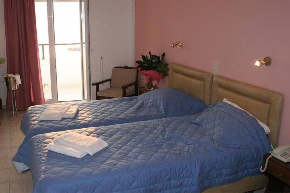 A hotel room with two beds, a chair, a plant, and a phone on the nightstand.