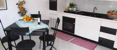 Uma cozinha compacta com armários brancos, bancada preta e um espaço de refeições com mesa e cadeiras.