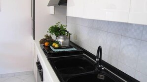 A kitchen with a black countertop, a sink, and a stove. There is a plant on the counter and a kettle. - Come In Sicily - Beachfront Sant'Alessio (Sant'Alessio Siculo)