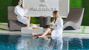 Two individuals relaxing by a poolside lounge area with a logo and text indicating a hotel name. - The Aliante Hotel (Malang)