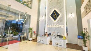 A hotel reception area with a marble wall, a logo, and a reception desk. - The Aliante Hotel (Malang)