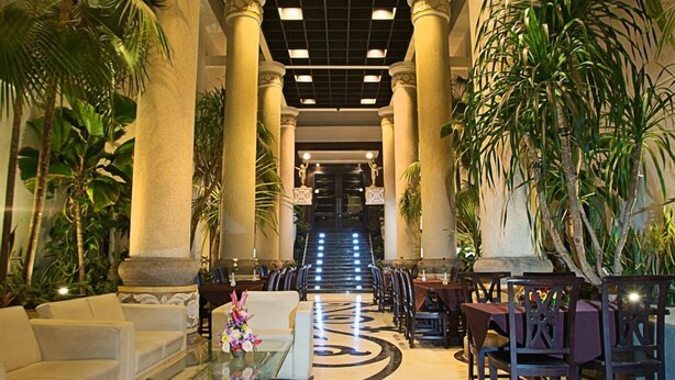 A lobby with a central staircase, flanked by columns and palm trees, leading to a higher floor. - The Aliante Hotel (Malang)
