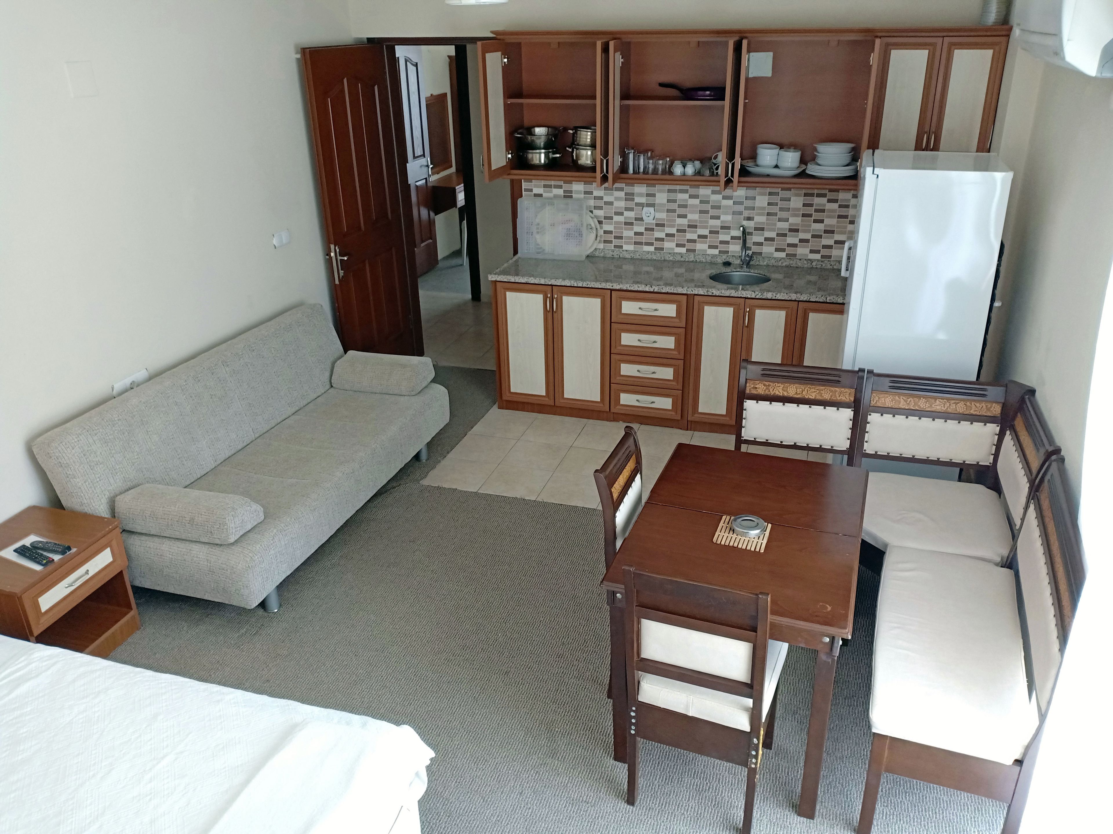 A compact living space with a kitchenette, a sofa, a dining table with chairs, and a bed.