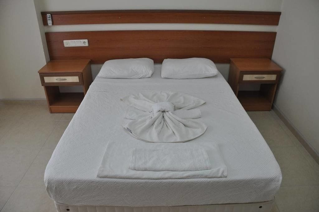 Un llit ben fet amb una disposició de tovalloles, panell de fusta al capçal i taules de nit amb calaixos.