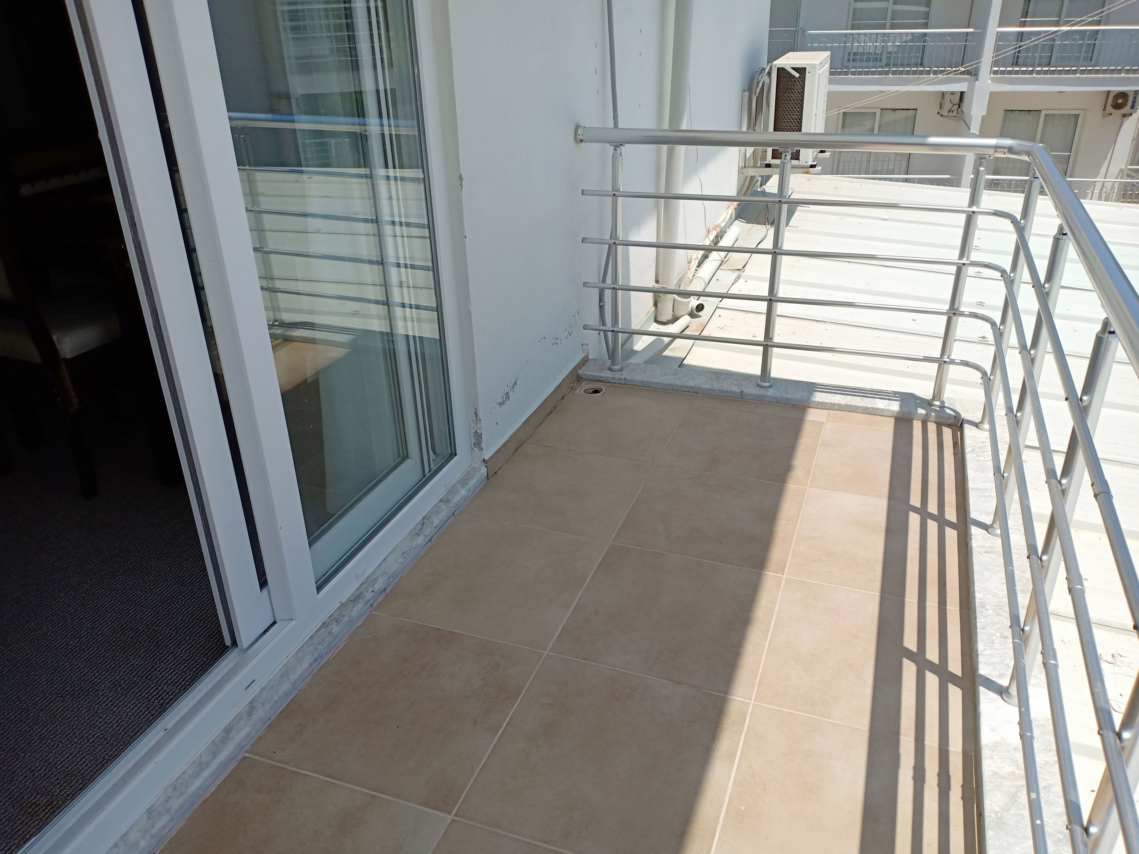 A balcony with a metal railing, a sliding glass door, and a tiled floor.