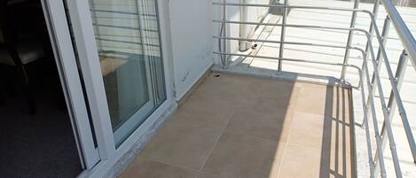 A balcony with a metal railing, a sliding glass door, and a tiled floor.