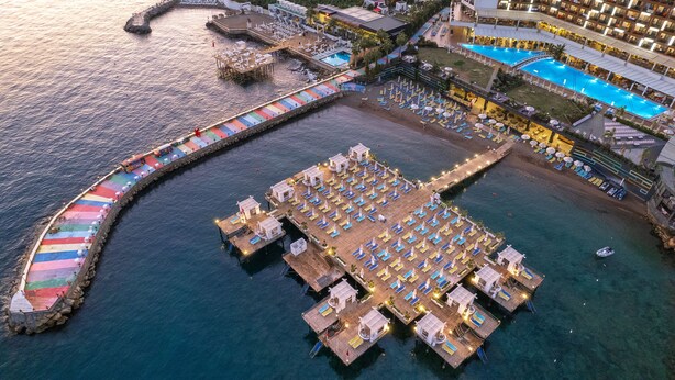 Vue aérienne d’un hôtel situé au bord de l’eau, avec une jetée, plusieurs piscines et des chaises longues.