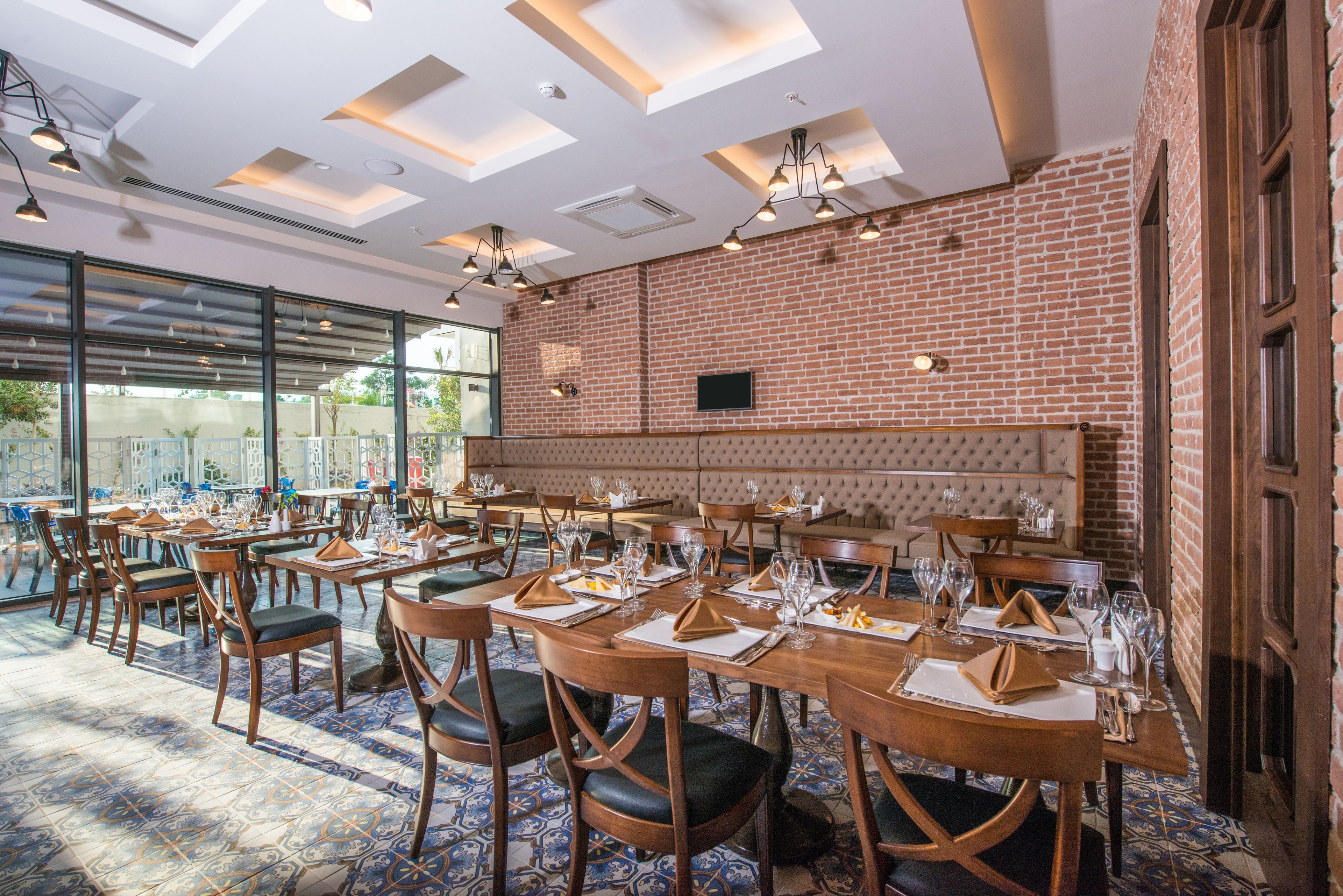 A restaurant with brick walls, wooden tables, and chairs, and a large window providing a view outside.