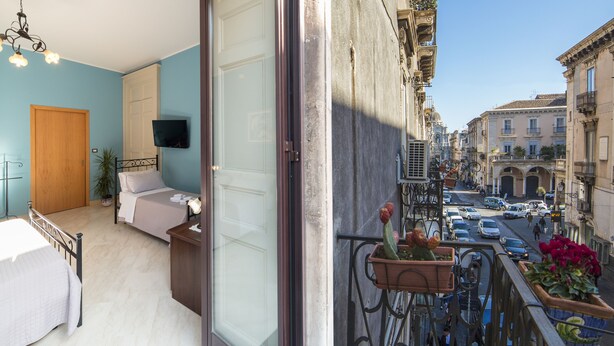 A bedroom with a bed, a TV, and a balcony with potted plants. - Catania Inn (Catania)
