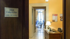 A hotel corridor with a reception desk, a sign for B&B Catania Inn, and a dining area in the background. - Catania Inn (Catania)