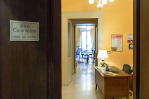 Corridoio di un hotel con una reception, una segnaletica per B&B Catania Inn e una sala da pranzo sullo sfondo.