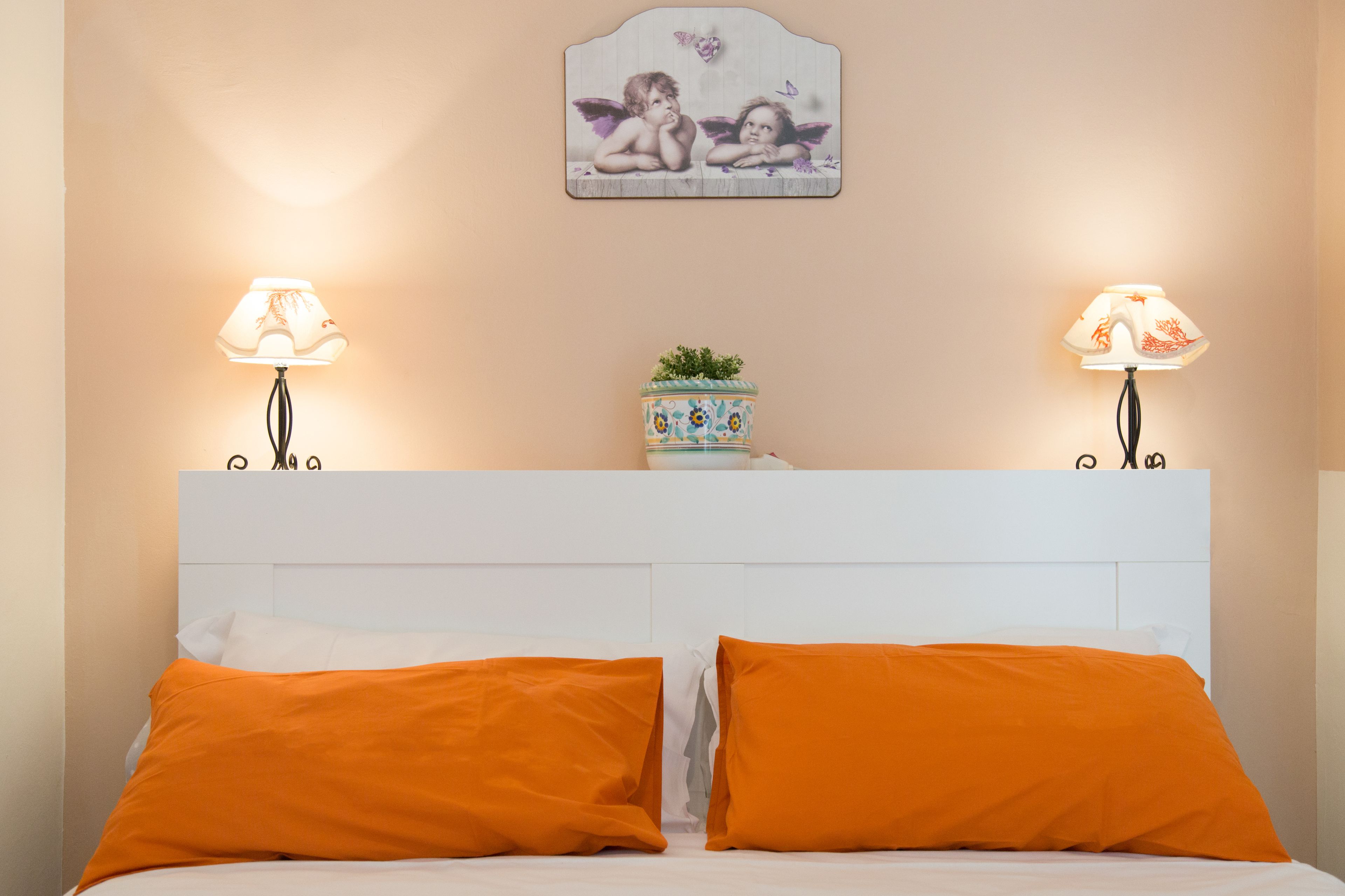 A neatly made bed with two orange pillows and a white headboard.