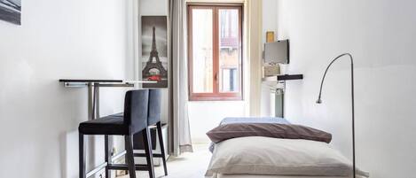 A compact room with a bed, a desk with a chair, a TV on a stand, and a window with a view of the Eiffel Tower.