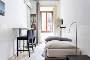 Una camera compatta con un letto, una scrivania con una sedia, una TV su un supporto e una finestra con vista sulla Torre Eiffel.