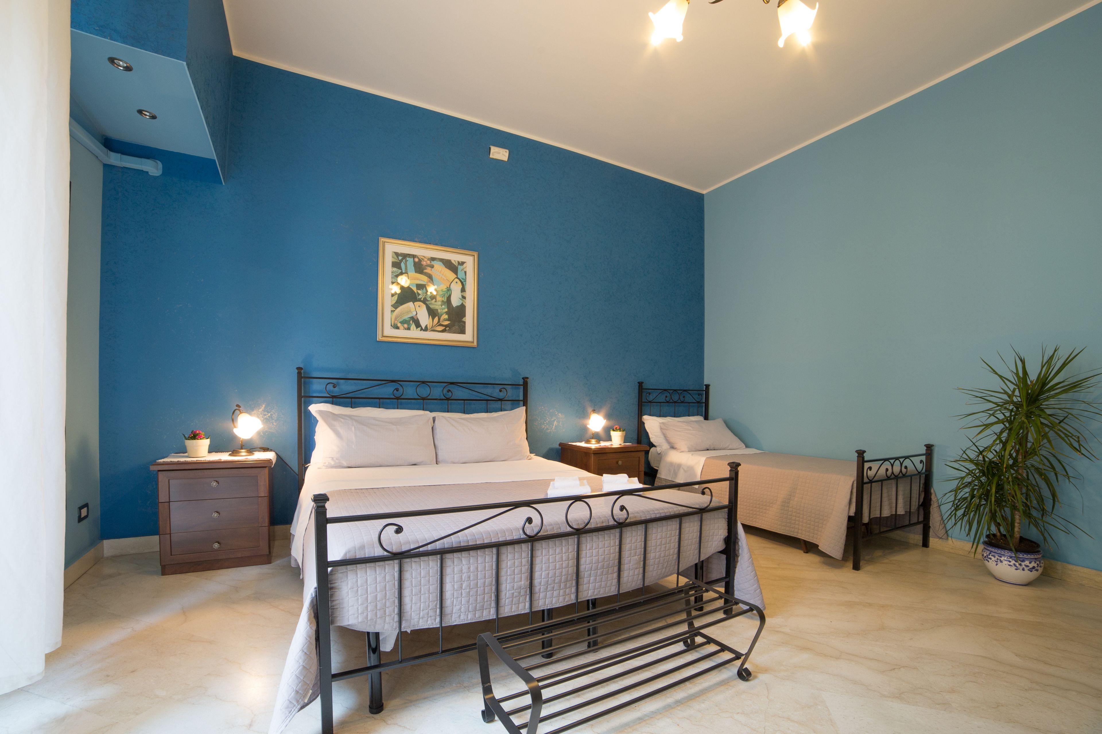 A bedroom with a bed, bedside tables, a nightstand, a potted plant, and a ceiling light fixture.