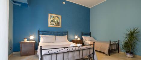 A bedroom with a bed, bedside tables, a nightstand, a potted plant, and a ceiling light fixture.