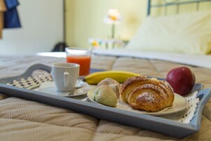A breakfast tray with croissants, a banana, an apple, a cup of coffee, and a glass of orange juice on a bed.