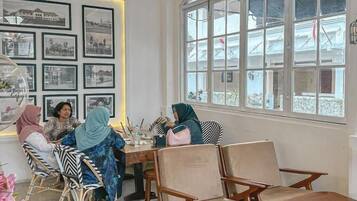 Una habitación con un ventanal arqueado grande, una pared con cuadros enmarcados y un grupo de personas sentadas en una mesa.