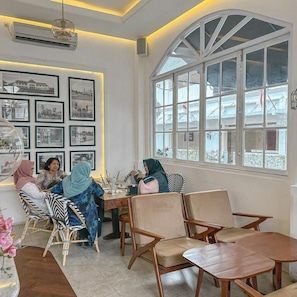 Una habitación con un ventanal arqueado grande, una pared con cuadros enmarcados y un grupo de personas sentadas en una mesa.