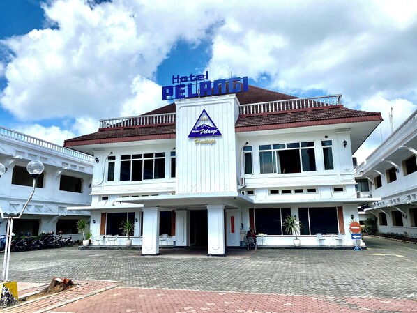 Hotel Pelangi con un letrero llamativo, un techo de tejas y un área de entrada empedrada.