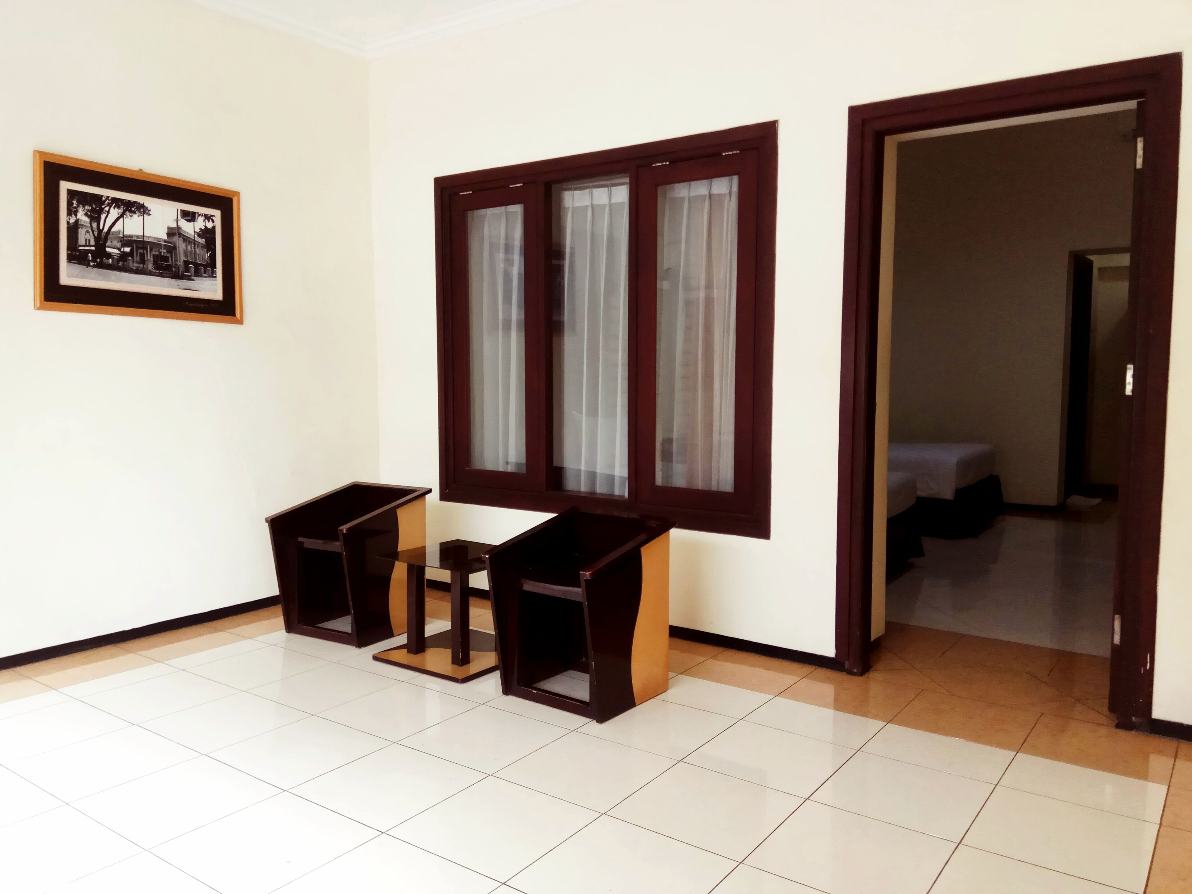 Um quarto com soalho em mosaico, uma mesa de madeira com cadeiras, uma janela com cortinas e um quadro na parede.