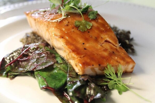 A plate with a piece of salmon, greens, and a garnish. - King Hill Inn & Kitchen (New London)