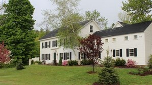 A two-story white house with black shutters, surrounded by a well-maintained lawn and various trees. - King Hill Inn & Kitchen (New London)