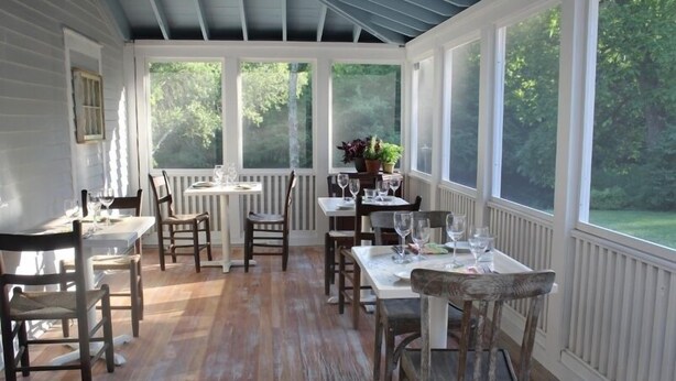 A covered dining area with wooden flooring, white walls, and large windows offering a view of the outdoors. - King Hill Inn & Kitchen (New London)