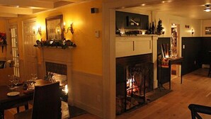 A cozy living room with a fireplace, wooden flooring, and a dining area with a table and chairs. - King Hill Inn & Kitchen (New London)