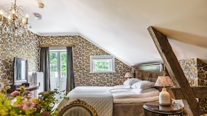 A bedroom with a bed, a table with a lamp, a chair, and a window with curtains.