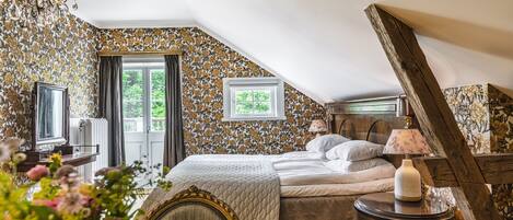 Een slaapkamer met een bed, een tafel met een lamp, een stoel en een raam met gordijnen.