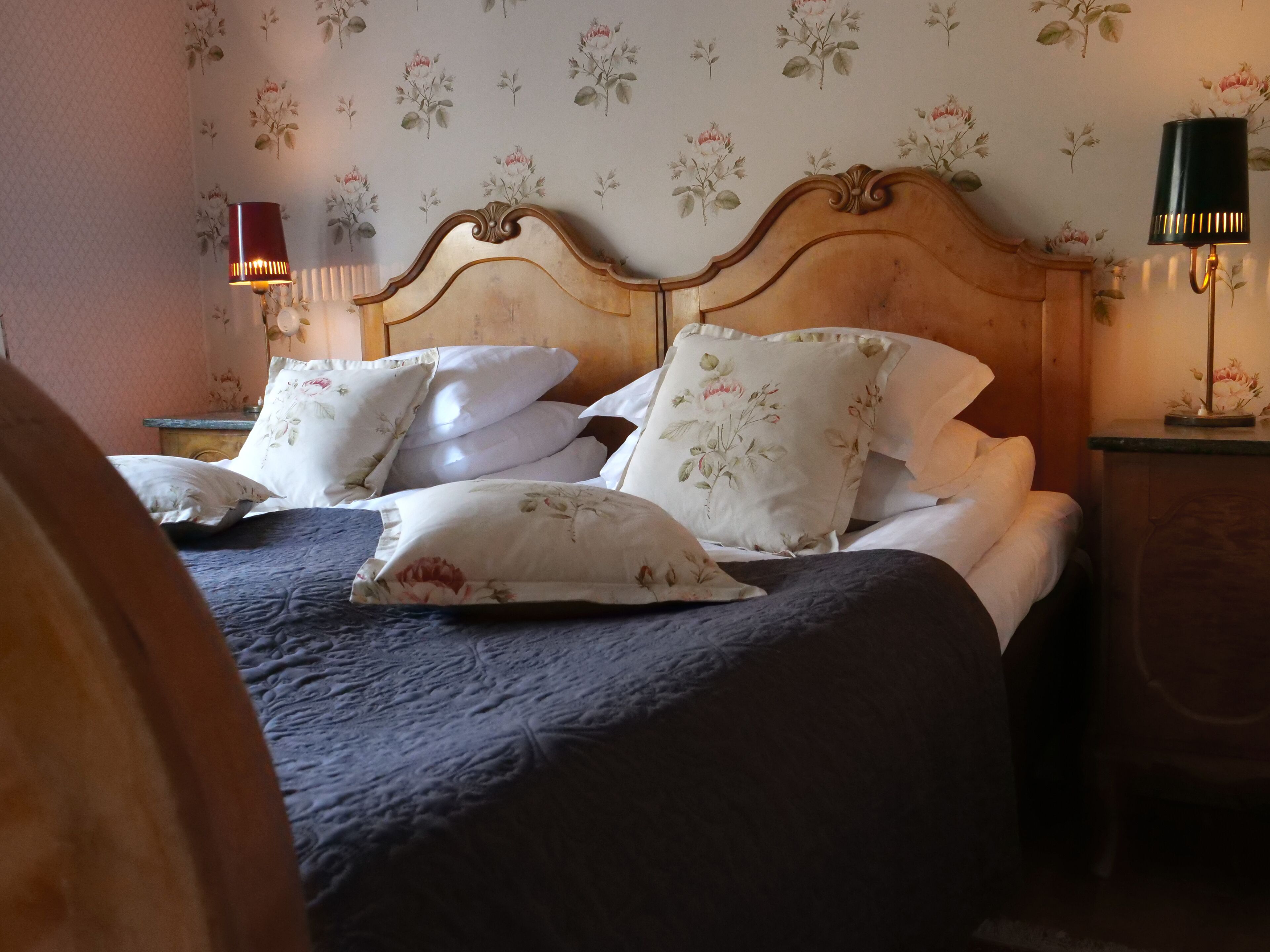 A bed with floral bedding and multiple pillows, a wooden headboard, and two bedside lamps.