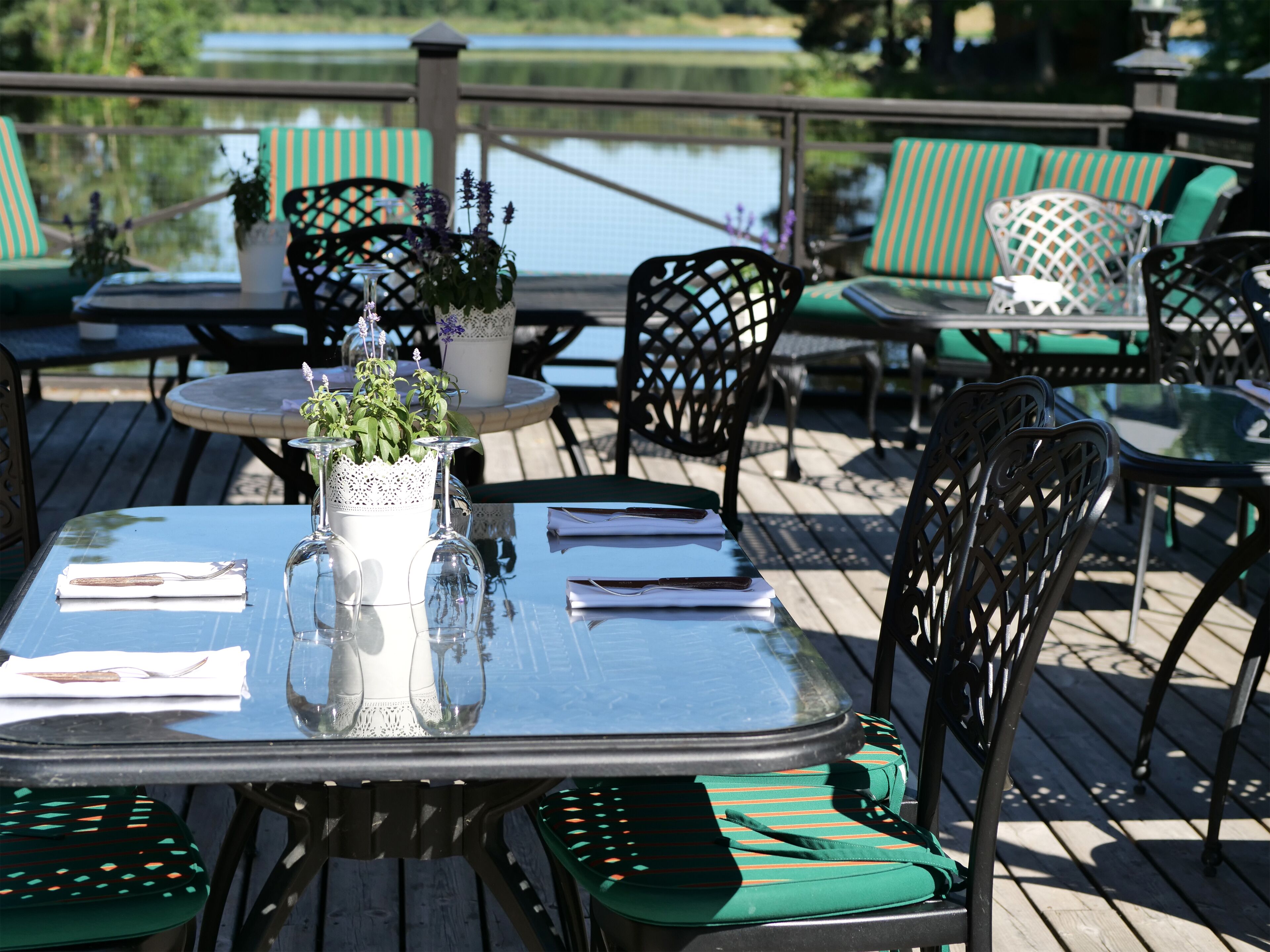 An outdoor dining area with tables and chairs, a decorative vase with flowers, and a view of a body of water.