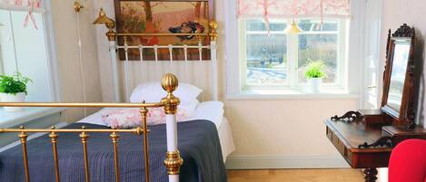 A bedroom with a bed, a window with a view, a red chair, and a painting on the wall.