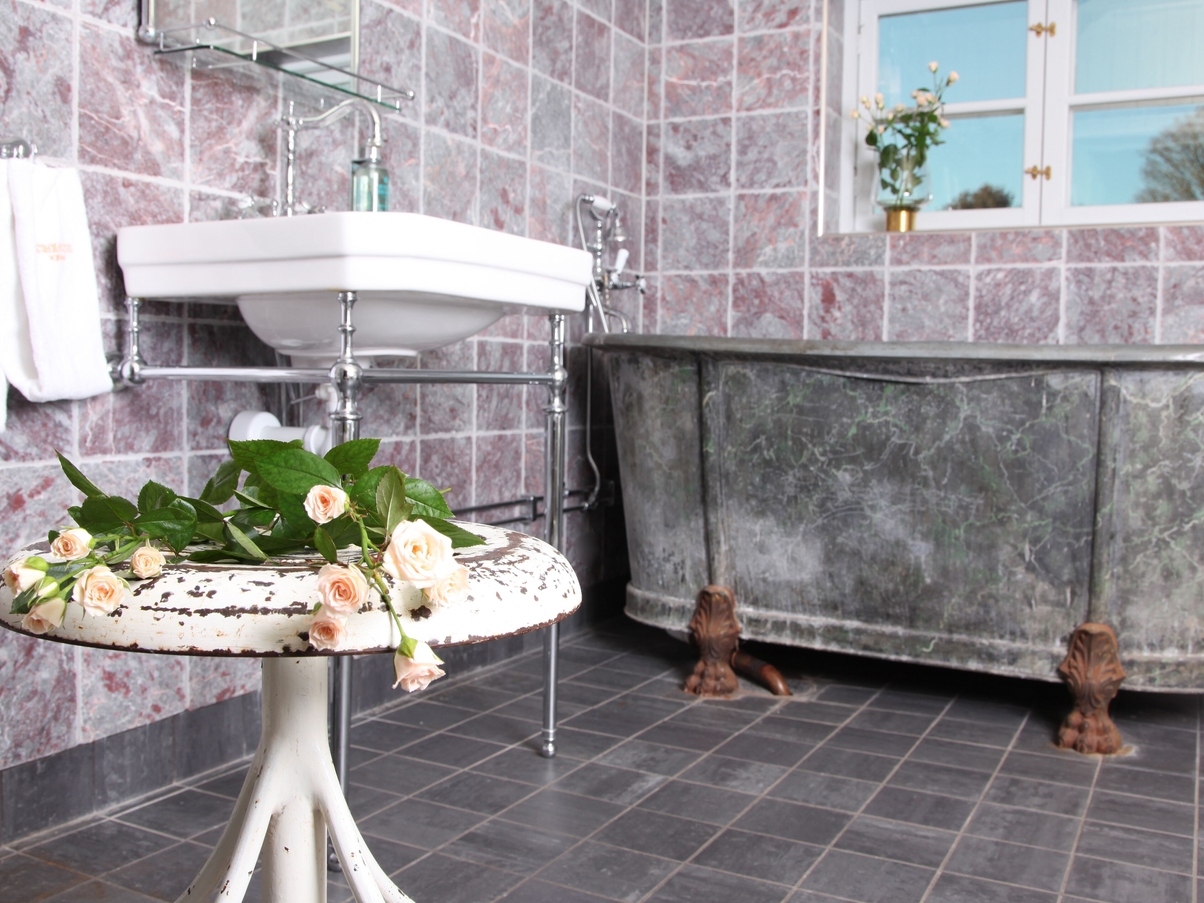 Een badkamer met een witte wastafel, een bad en een decoratietafel met bloemen.