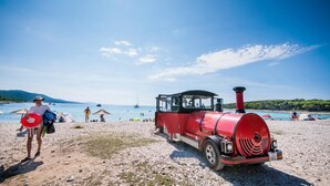 A red train on a beach with people and boats in the background. - Hotel Agava (Bozava)