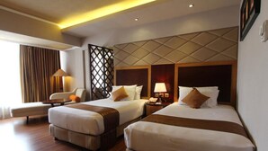 A hotel room with two beds, a sofa, a desk, and a lamp. - Regent's Park Hotel (Malang)