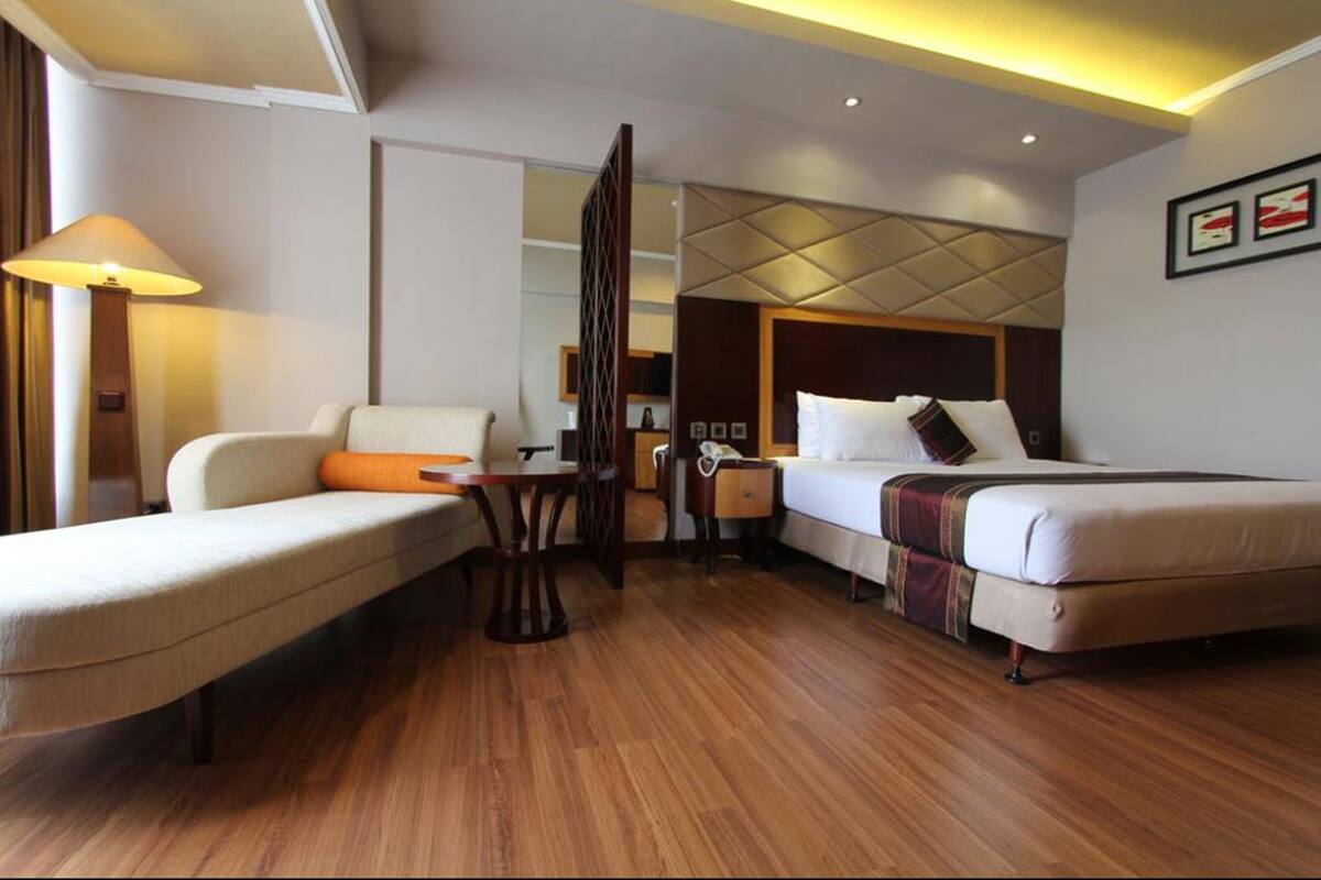 A hotel room with a bed, a sofa, a desk, and a lamp.