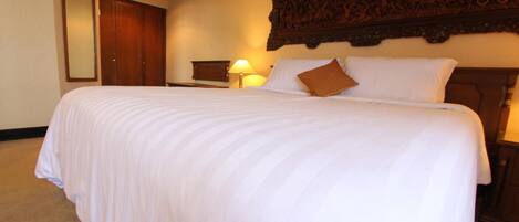 A hotel room with a large bed, a wooden headboard, a nightstand with a lamp, and a wardrobe.