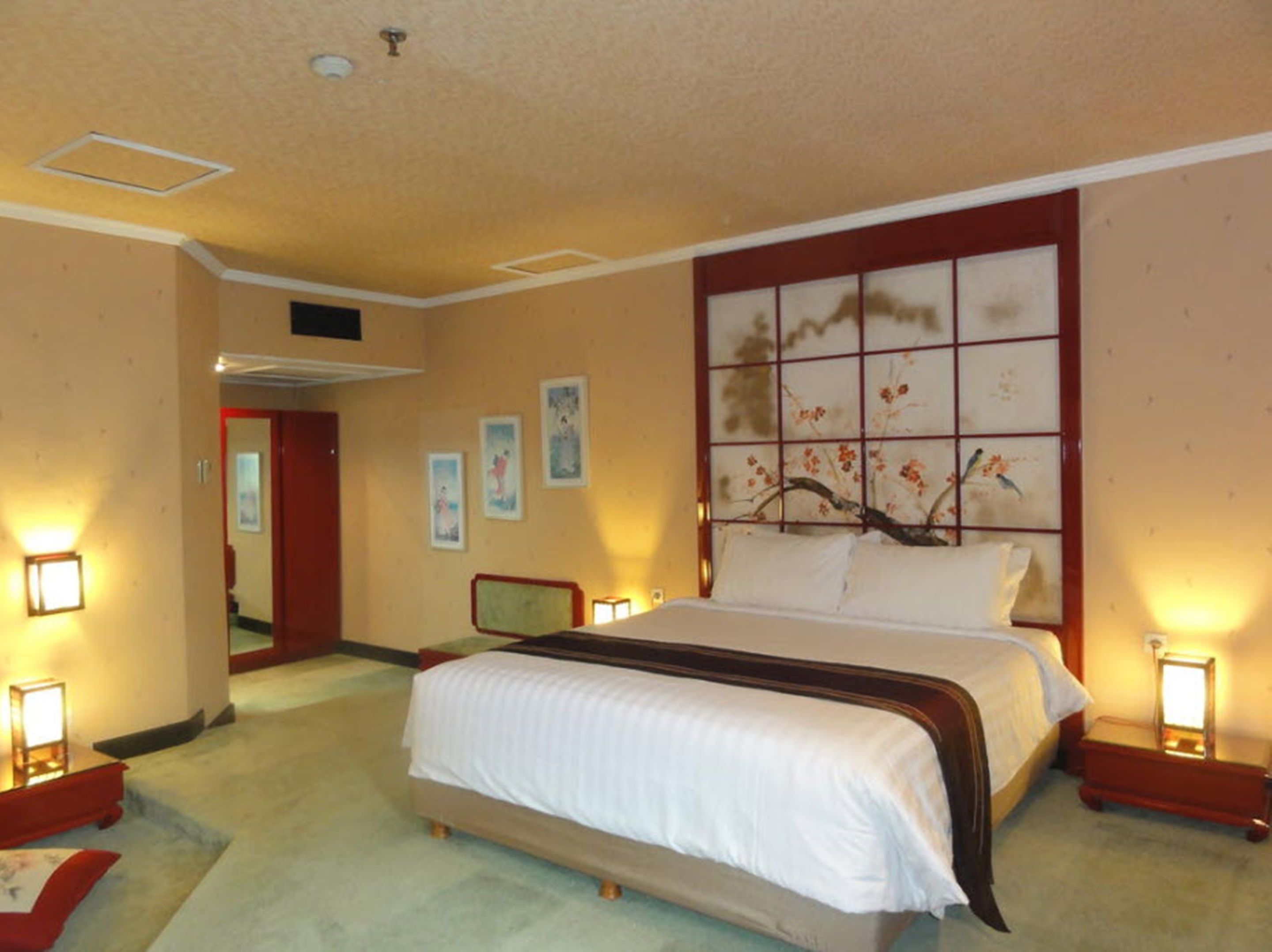 Habitación de hotel con una cama grande, cabecera de madera y un panel decorativo en la pared. Hay dos mesitas de noche con lámparas.