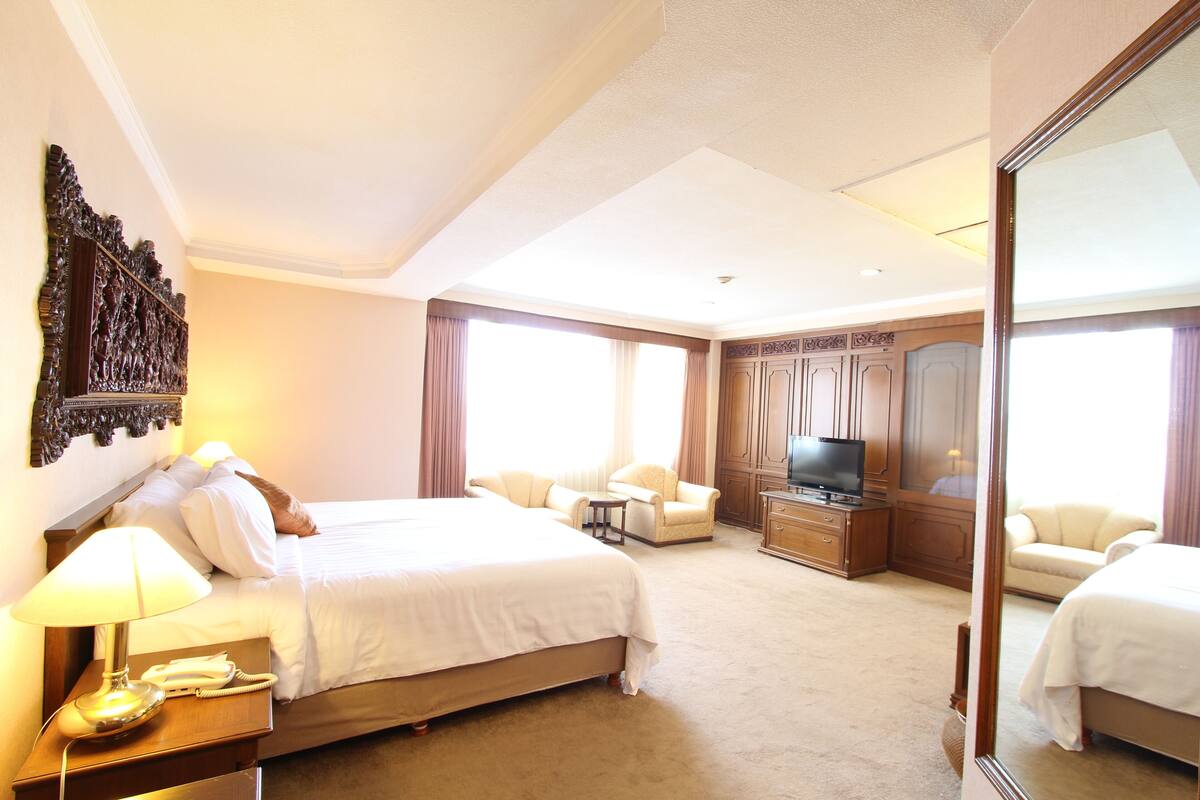 A hotel room with a large bed, a television, a desk with a lamp, and a mirror.