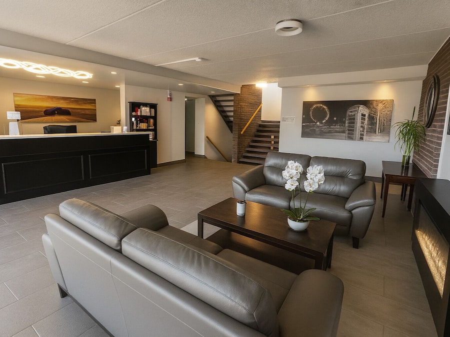 Ein modernes Wohnzimmer mit einer Couch, einem Couchtisch und einem Kamin. Im Hintergrund ist eine Rezeption mit einer Theke und eine Treppe zu sehen.