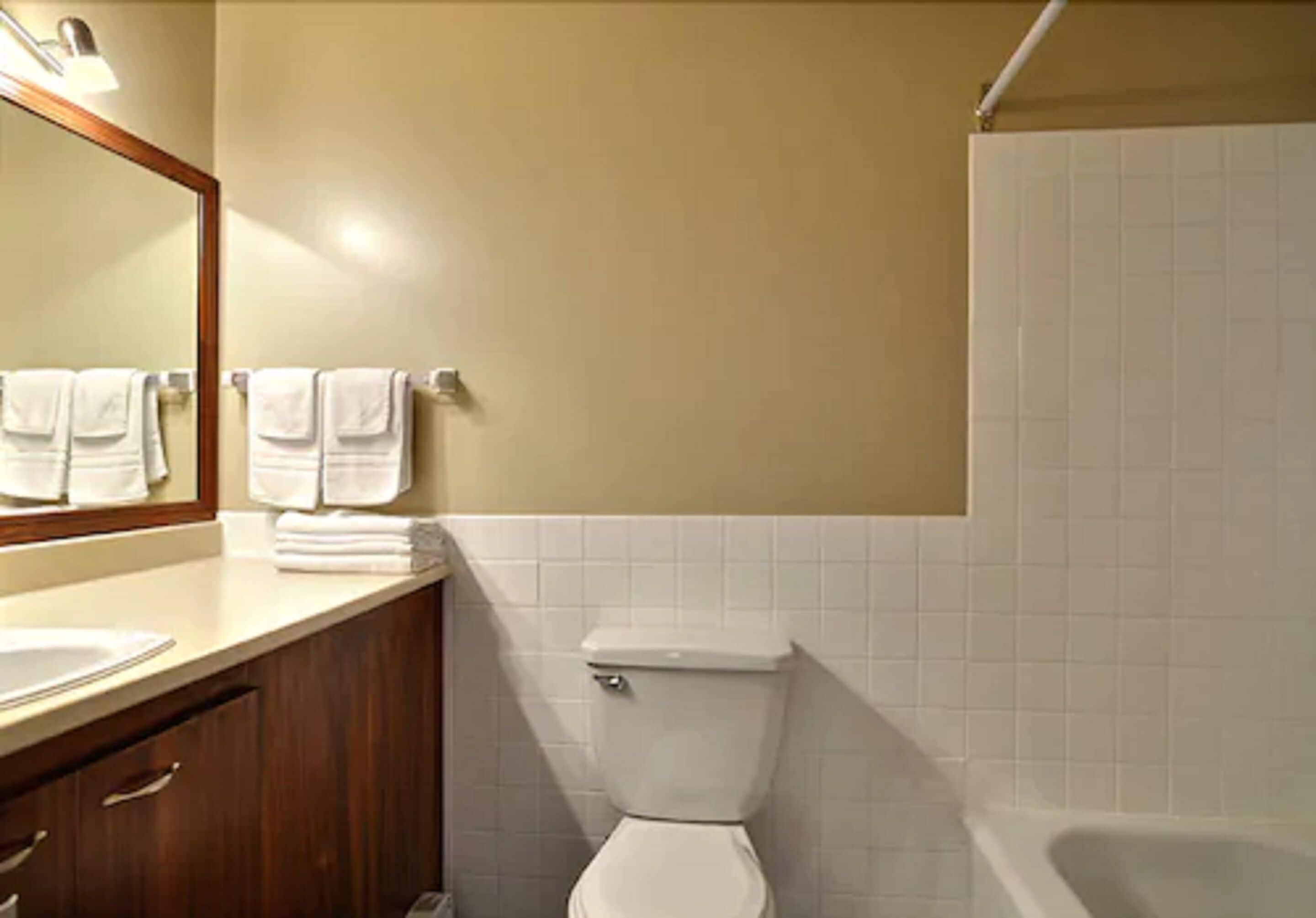 A bathroom with a toilet, sink, and bathtub. There are towels hanging on the wall.