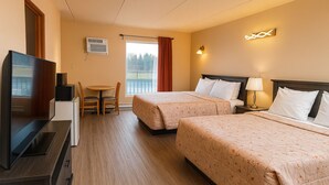Quarto de hotel com duas camas, televisão, escrivaninha e janela com vista para árvores.