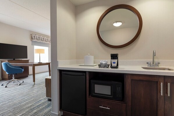 A hotel room with a desk, chair, microwave, coffee maker, and a large mirror.