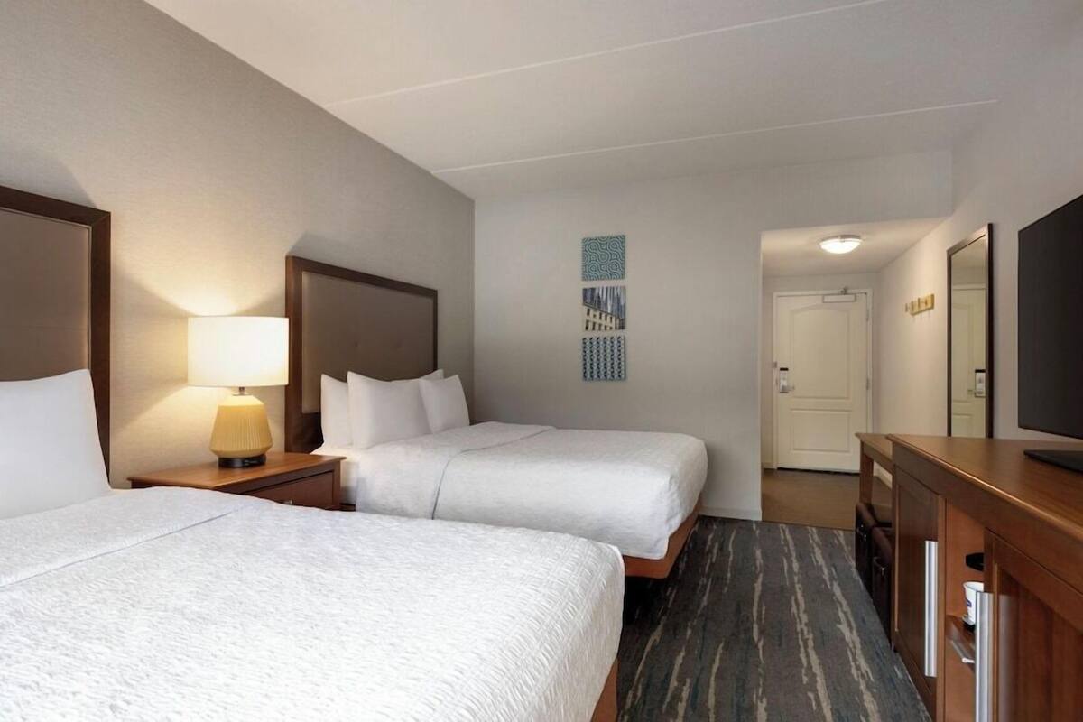 A hotel room with two beds, a desk, a TV, and a door leading to another room.