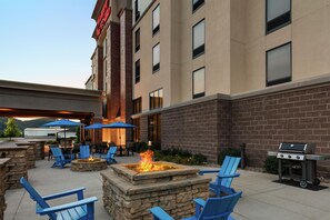 An outdoor patio with stone fire pit seating, a grill, and umbrellas. - Hampton Inn & Suites Pittsburgh/Harmarville (Pittsburgh)