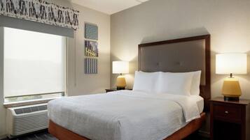 Quarto de hotel com uma cama grande, duas luminárias de cabeceira, uma janela com persianas e uma parede com padrões decorativos.